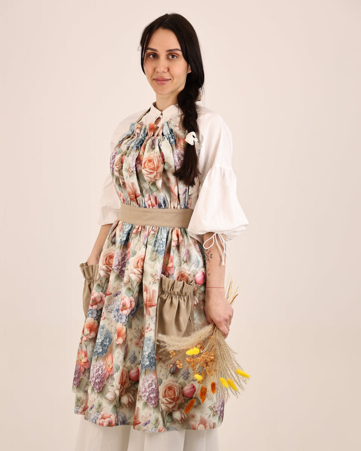 Woman wearing a floral apron over a white blouse with a beige background