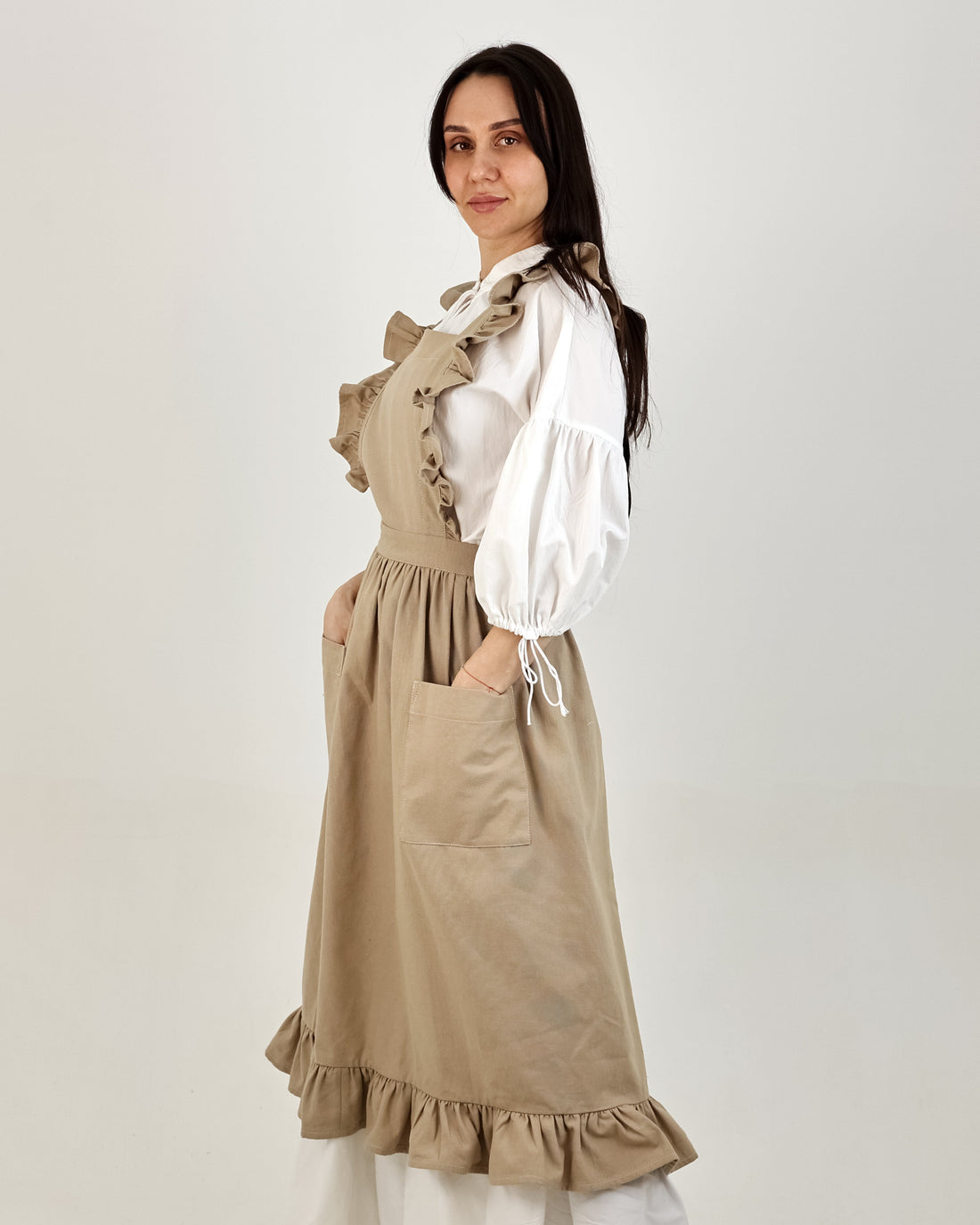 Woman wearing a beige dress with a white blouse against a plain background