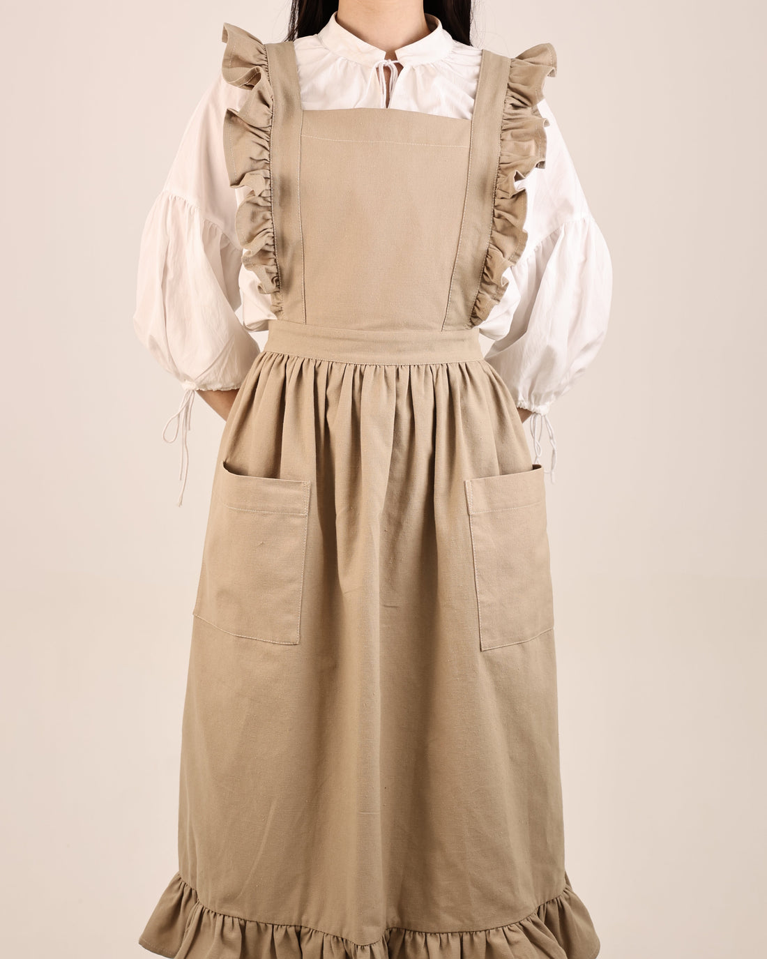 Person wearing a beige apron over a white blouse on a plain background