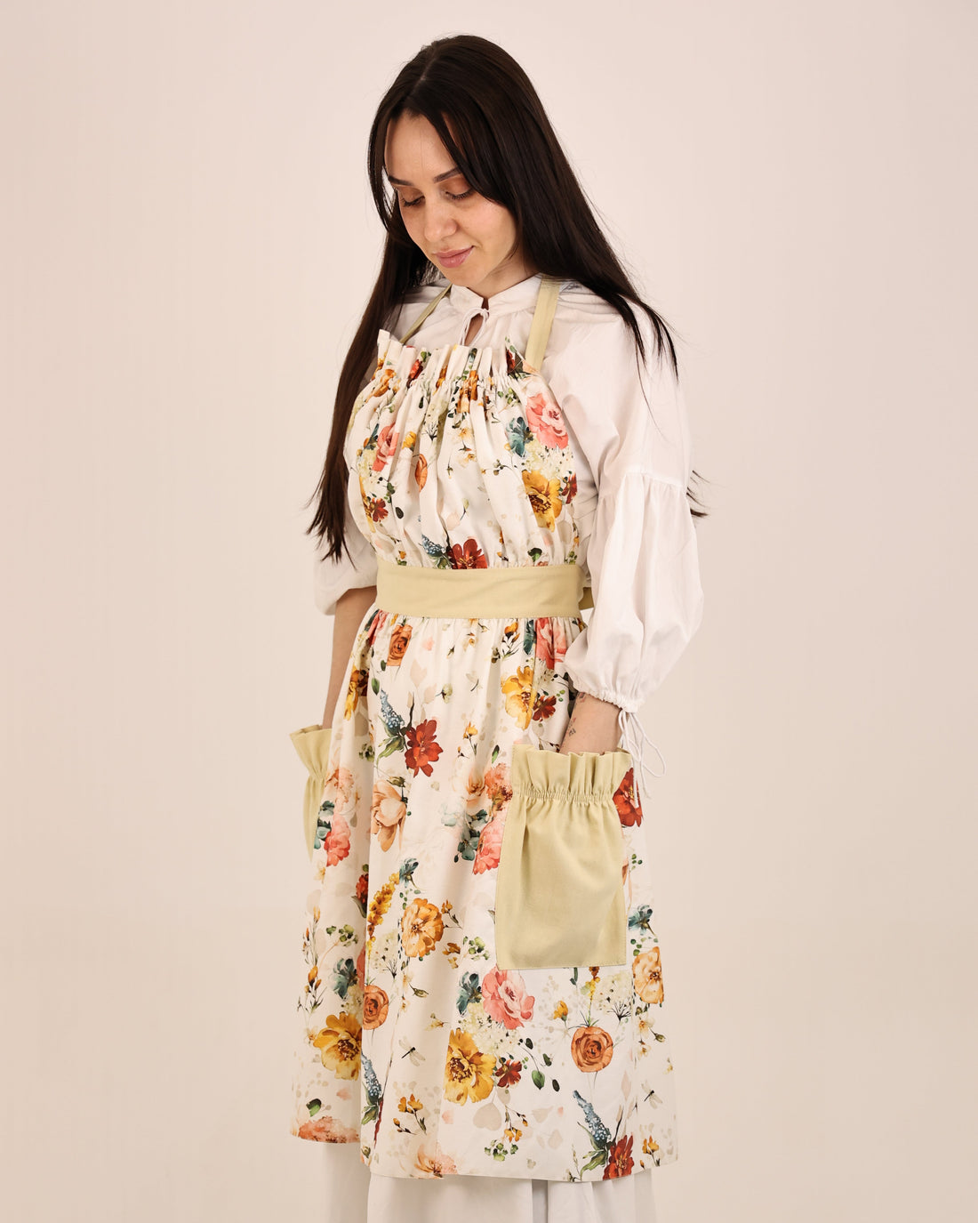 Woman wearing a floral apron over a white shirt on a beige background
