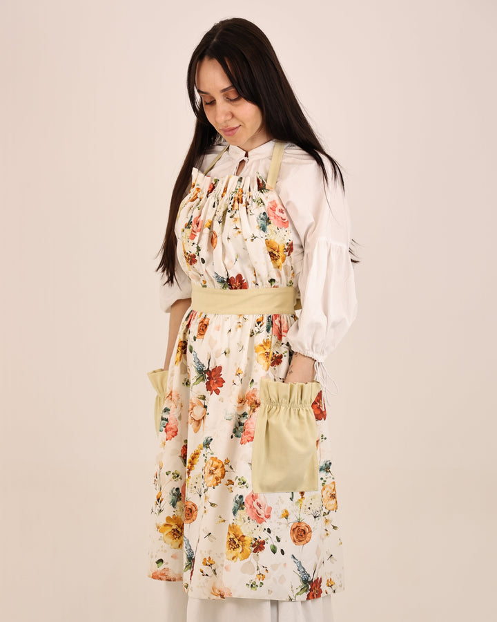 Woman wearing a floral apron over a white shirt on a beige background