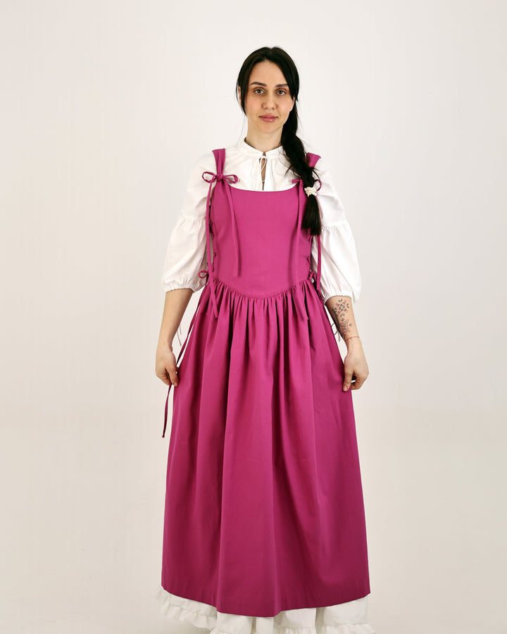 Woman wearing a pink dress with a white blouse on a plain background