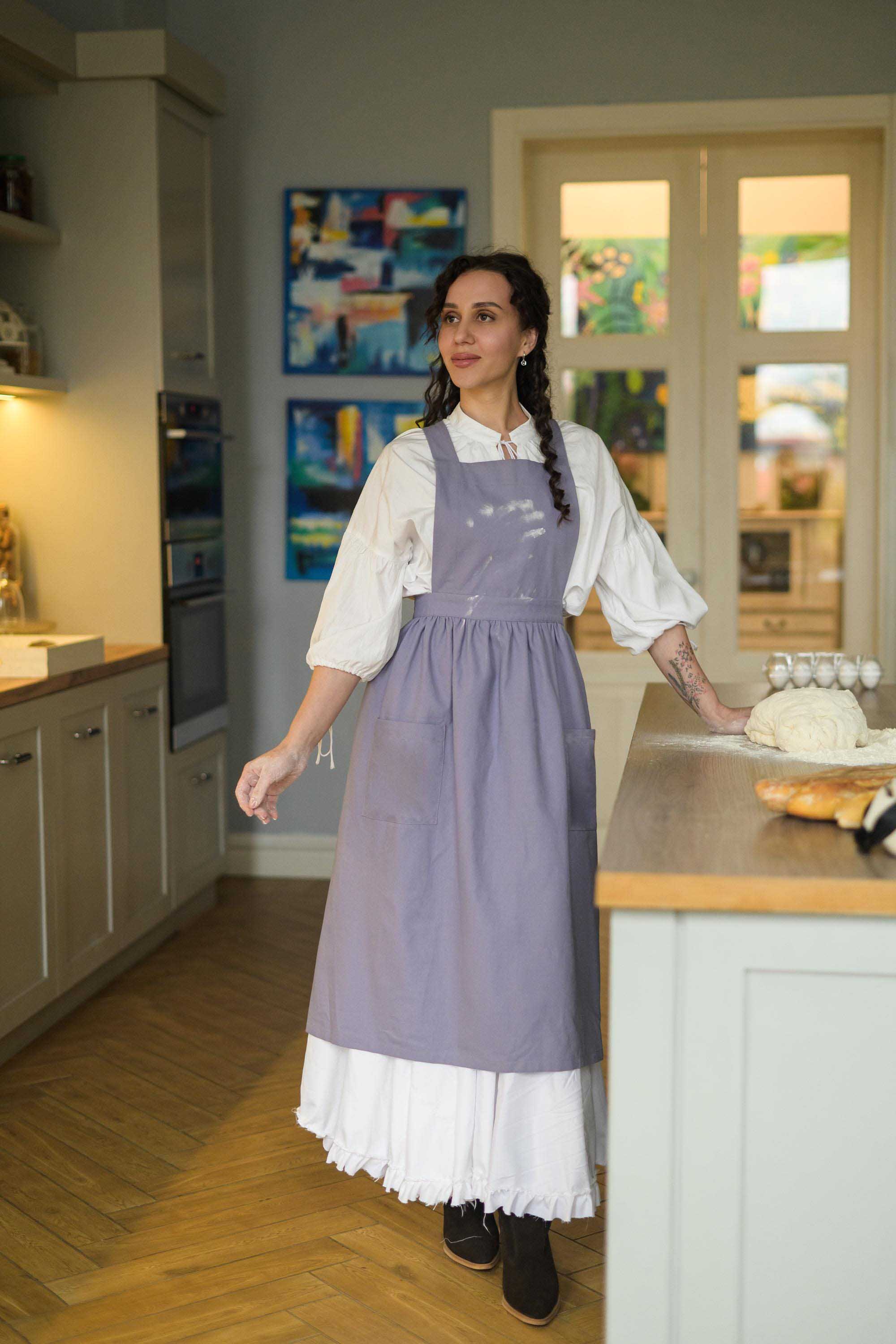 Woman in a kitchen wearing a purple apron and white shirt.