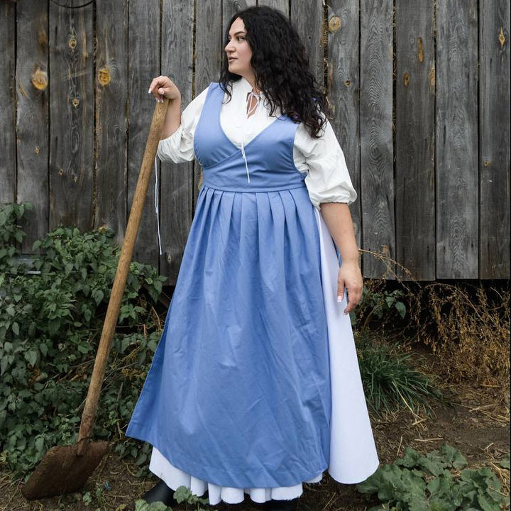 Woman in a blue dress holding a broom in front of a wooden fence.