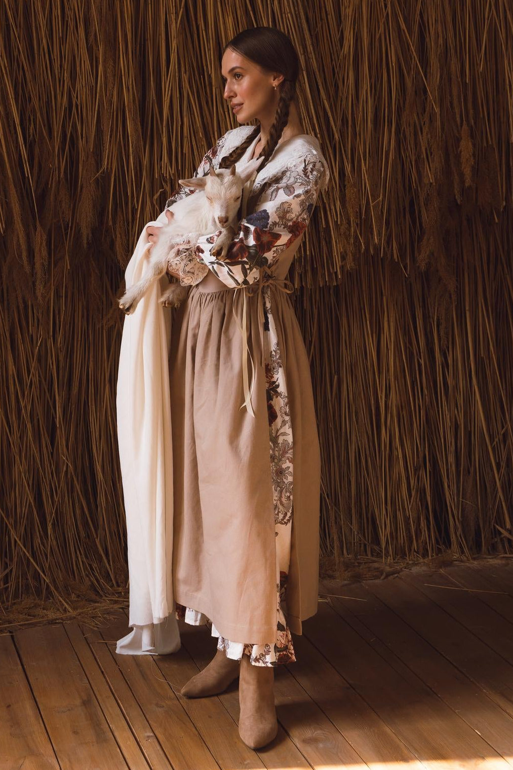 Woman in a long, light-colored apron standing in a room with straw walls and wooden floor.