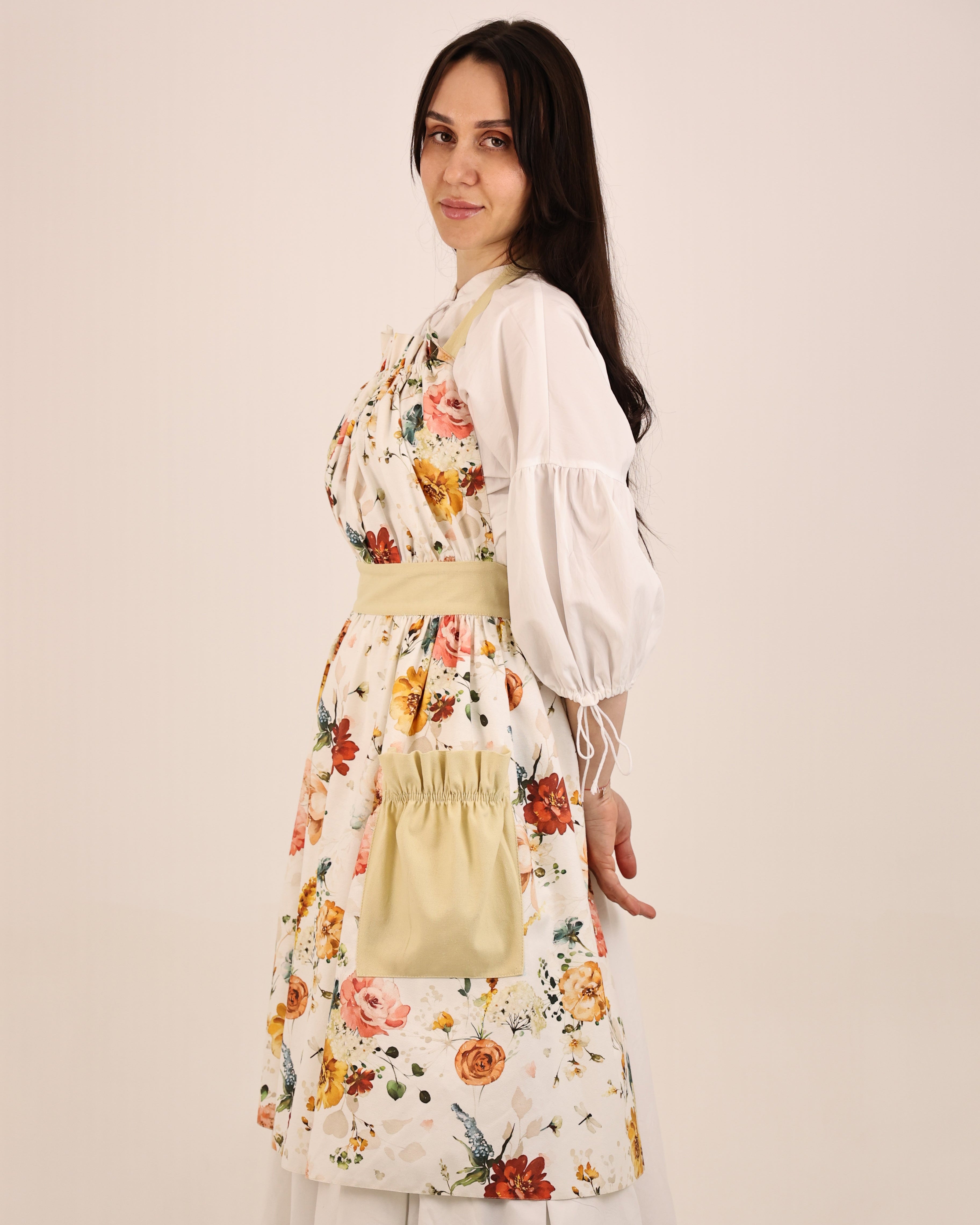 Woman wearing a floral apron over a white dress against a beige background