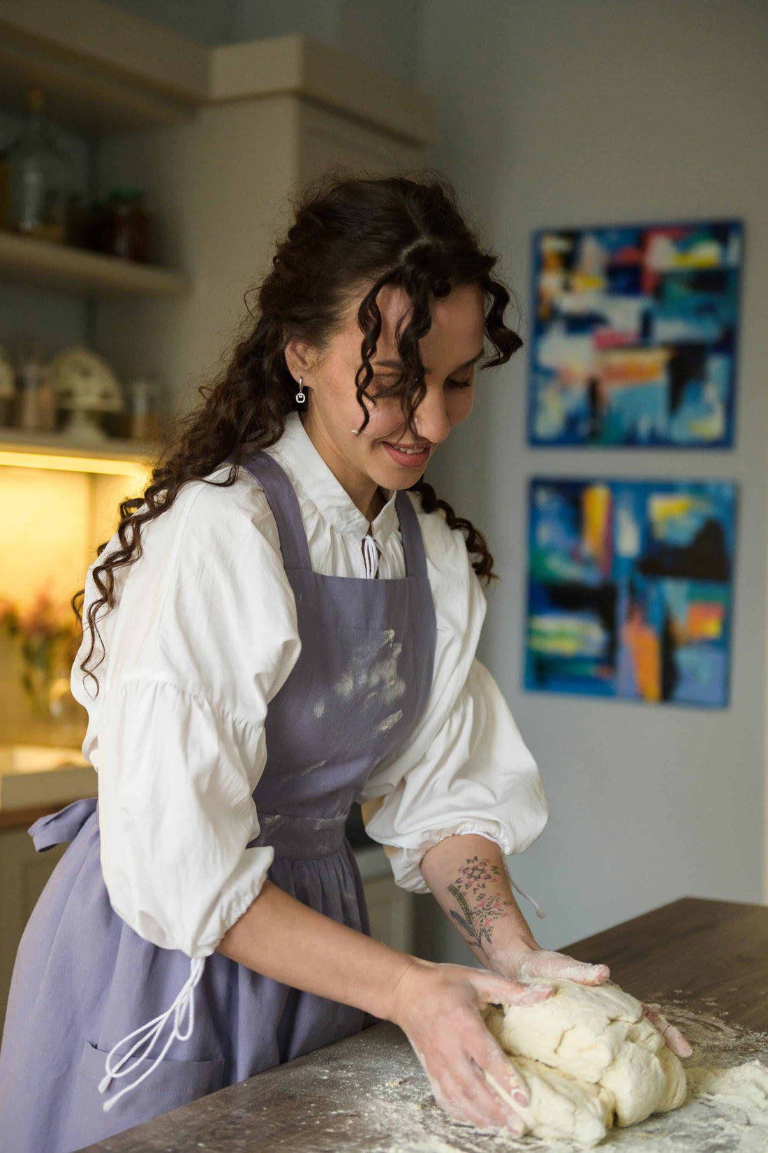 Woman in a kitchen kneading dough, with abstract art on the wall.