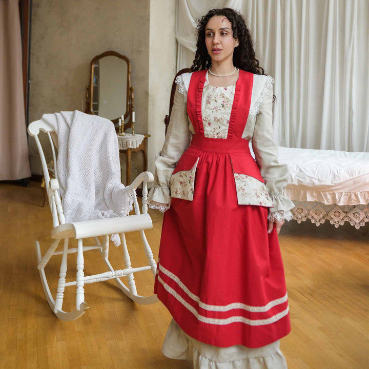Woman in a red and white dress standing in a room with a rocking chair and bed.