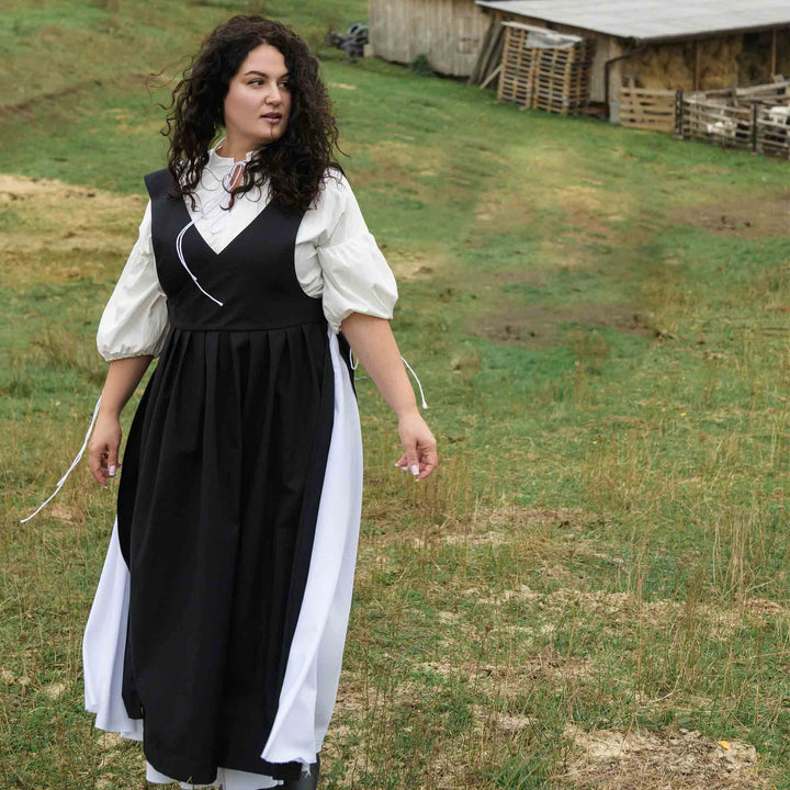 Woman in a black and white dress standing in a grassy field with a barn in the background.