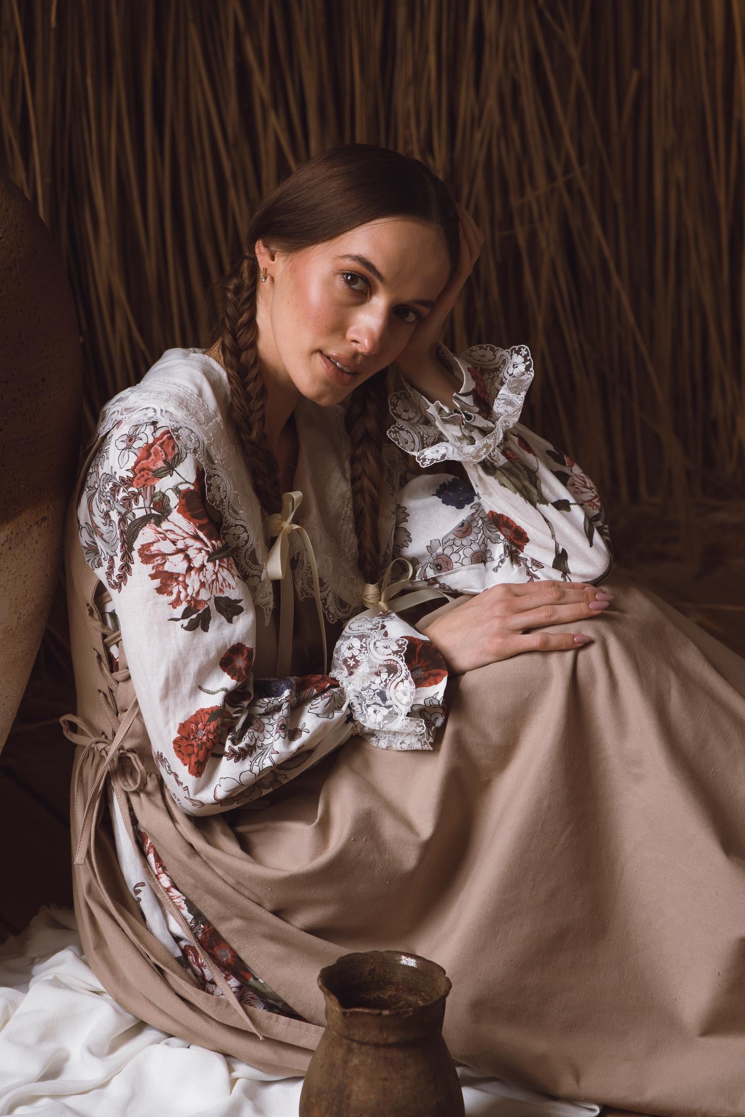 Woman in traditional embroidered blouse and skirt holding a baby in a rustic setting.
