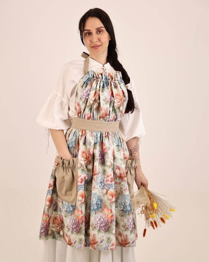 Woman wearing a floral apron over a white shirt with a beige background