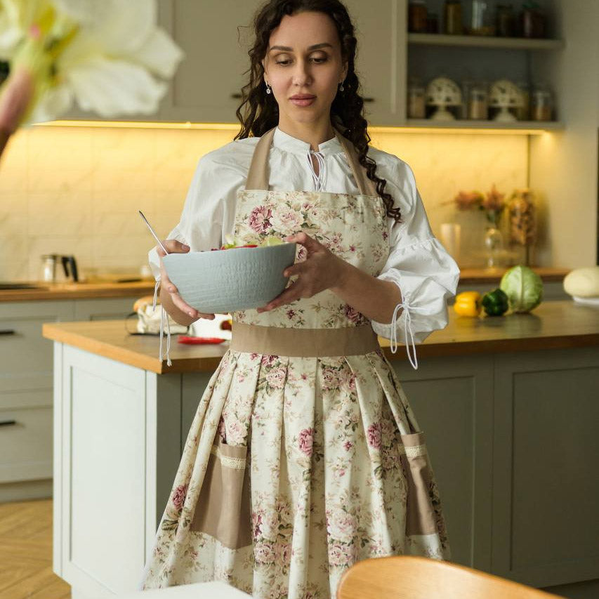 Woman in a kitchen holding a bowl, wearing a floral apron.