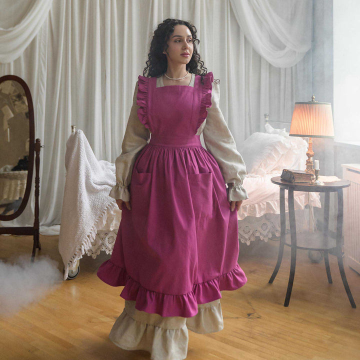 Woman in a vintage-style apron standing in a room with white curtains and a lamp.