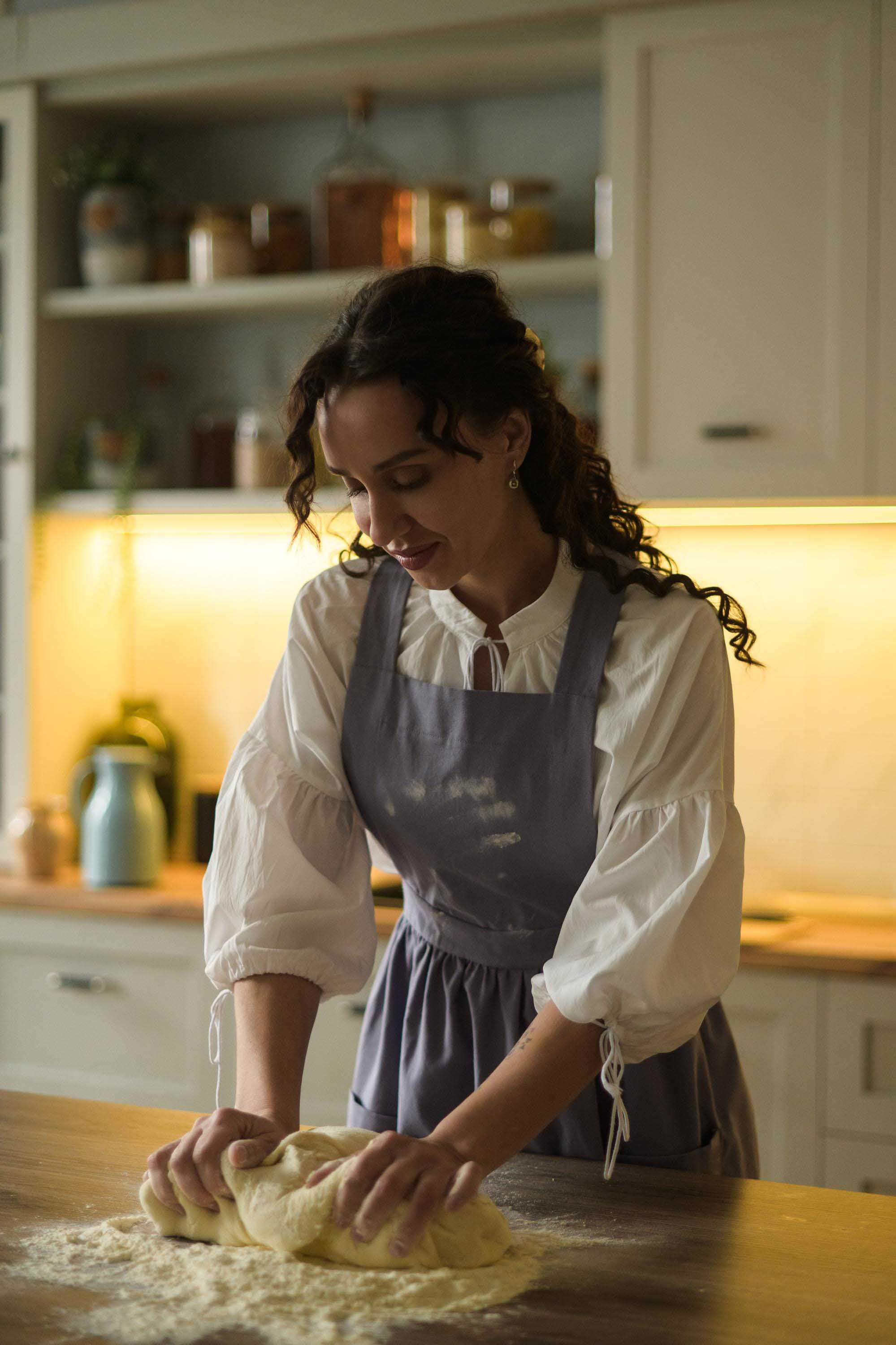 Woman in a kitchen kneading dough on a wooden table.